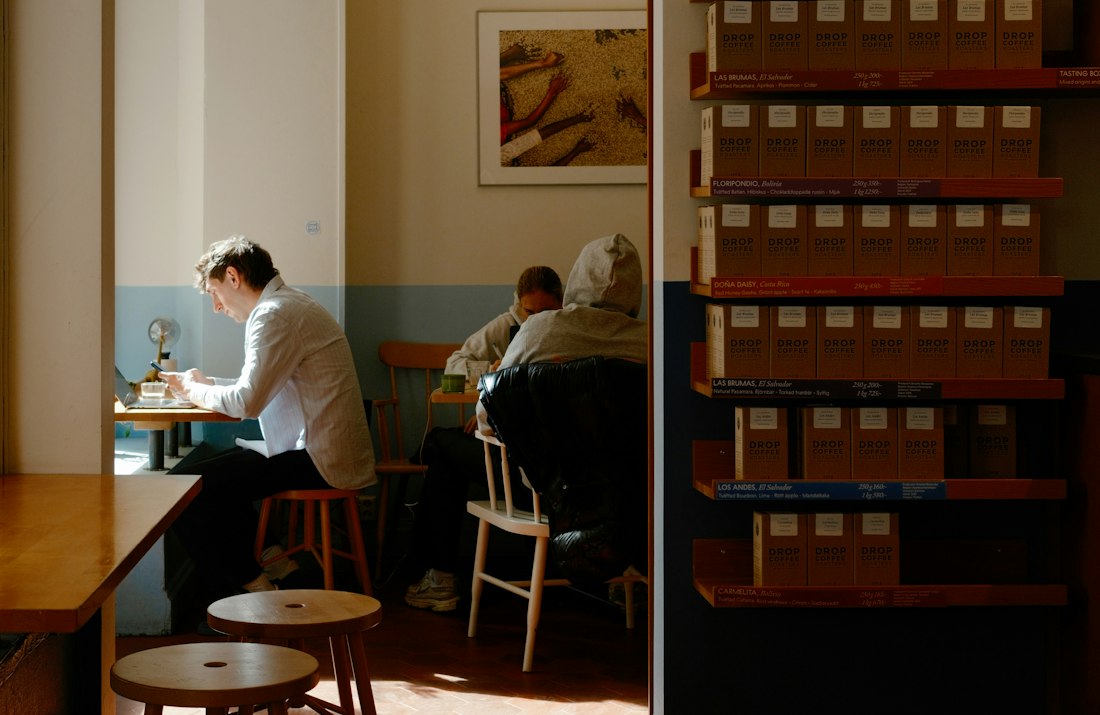 A man working on his laptop at a small table in a sunlit café